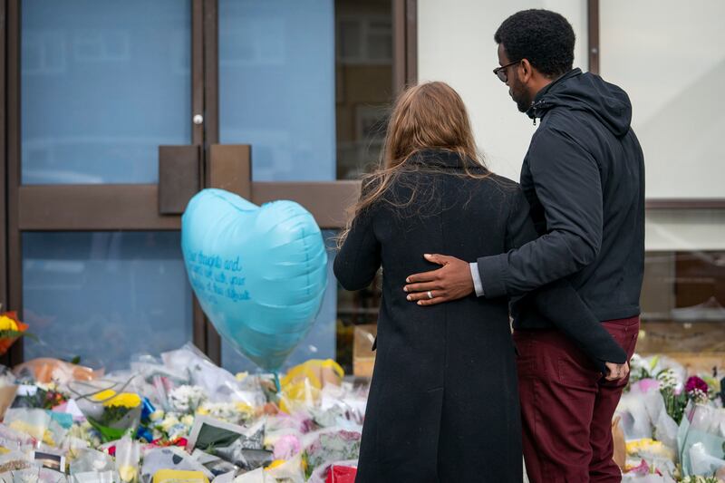 A daughter of SIr David Amess is comforted as she views flowers and tributes left for her late father. AP