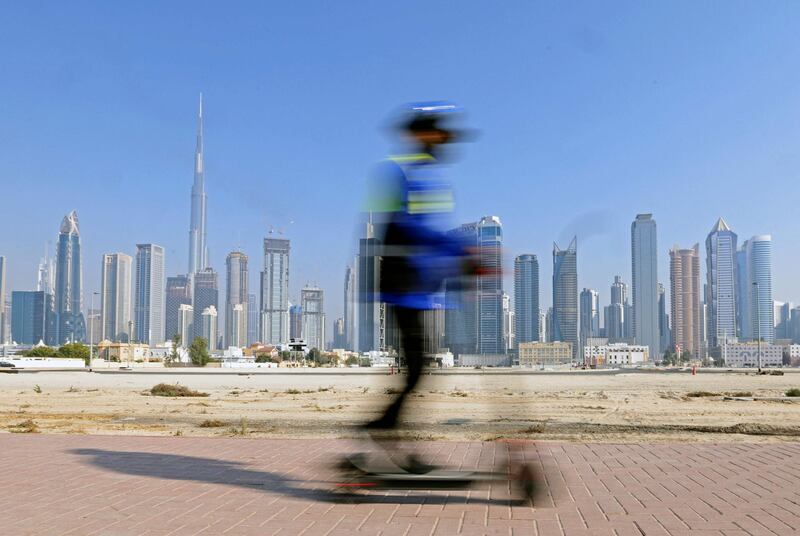 A man rides his electric scooter in Dubai backdropped by the Gulf emirate's highrise buildings on February 16, 2021.  / AFP / Karim SAHIB
