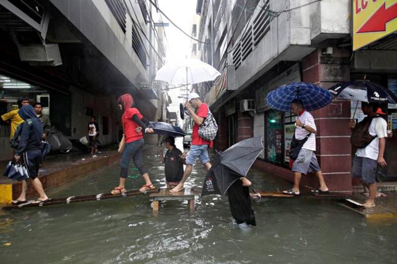 epa03830352 Filipinos walk on a wooden plank over floodwaters in Manila, Philippines 19 August 2013. The Philippines' weather bureau continues to track tropical storm Trami which has been estimated at 550 kilometers east of Batanes province in the northern Philippines, with maximum winds of 75 kilometers per hour. Metro Manila experienced flashfloods from heavy rains due to a southwest monsoon being enhanced by Trami, local media reports stated.  EPA/ROLEX DELA PENA