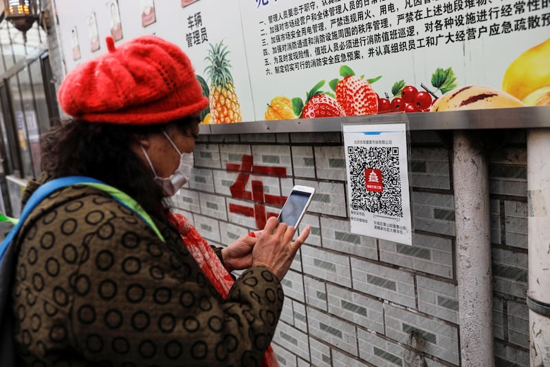 A woman scans a health QR code on her smartphone to register her visit to a market before crossing the entry checkpoint in Beijing, China. Reuters