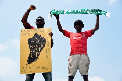 TOPSHOT - A protester gesture while holding placard as another holds up a scarf with the colours of the Nigerian national flag during a demonstration to protest against police brutality at Magboro, Ogun State in southwest Nigeria, on October 20, 2020. Authorities declared a 24-hour curfew in Nigeria's economic hub Lagos on October 20, 2020, as violence flared in widespread protests that have rocked cities across the country. / AFP / PIUS UTOMI EKPEI
