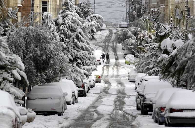 Jordanians walk past snow-covered cars and trees in Amman on January 10, 2013. The worst storms in a decade left swathes of Israel and Jordan under a blanket of snow and parts of Lebanon blacked out, bringing misery to a region accustomed to temperate climates. AFP PHOTO/KHALIL MAZRAAWI

