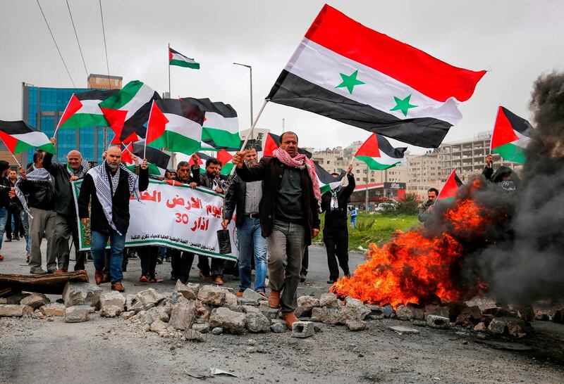 A man waves a Syrian national flag as others wave Palestinian flags behind him while marching during a demonstration marking "Land Day", near the Israeli Jewish settlement of Beit El in the occupied West Bank. AFP