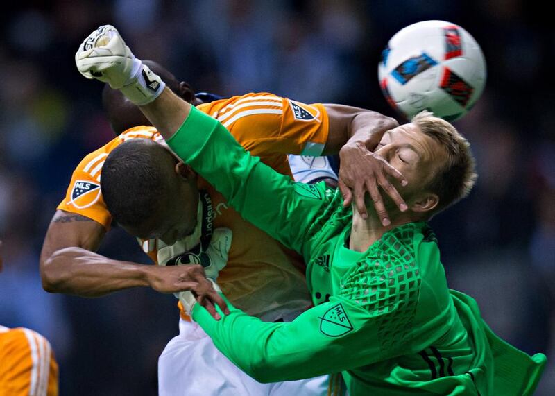 Houston Dynamo’s Ricardo Clark, left, gets his hand on the face of teammate and goalkeeper Joe Willis as Willis tries to punch the ball away from Vancouver Whitecaps’ Kekuta Manneh, rear, during the first half of an MLS soccer game in Vancouver, British Columbia. Darryl Dyck / The Canadian Press via AP