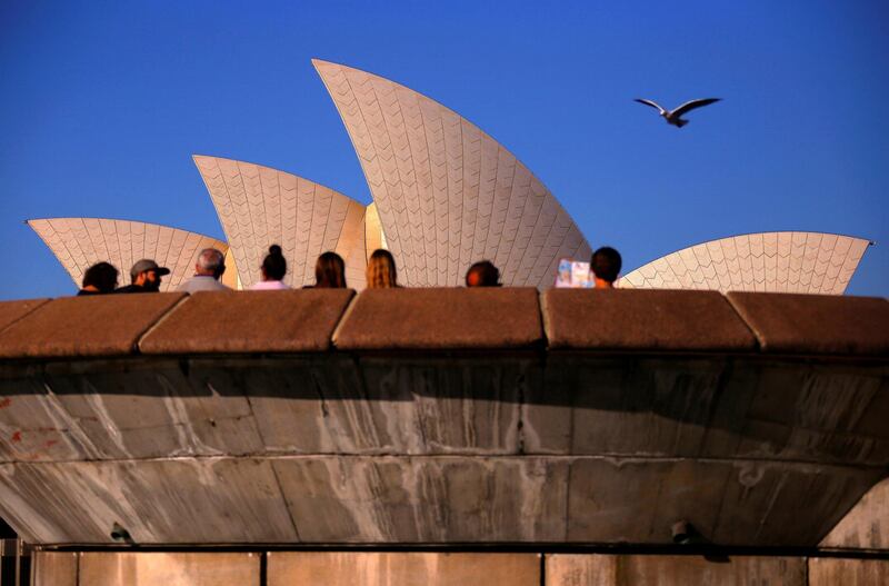 A seagull flies over tourists sitting on a concrete bench in front of the Sydney Opera House in central Sydney, Australia. David Gray/Reuters