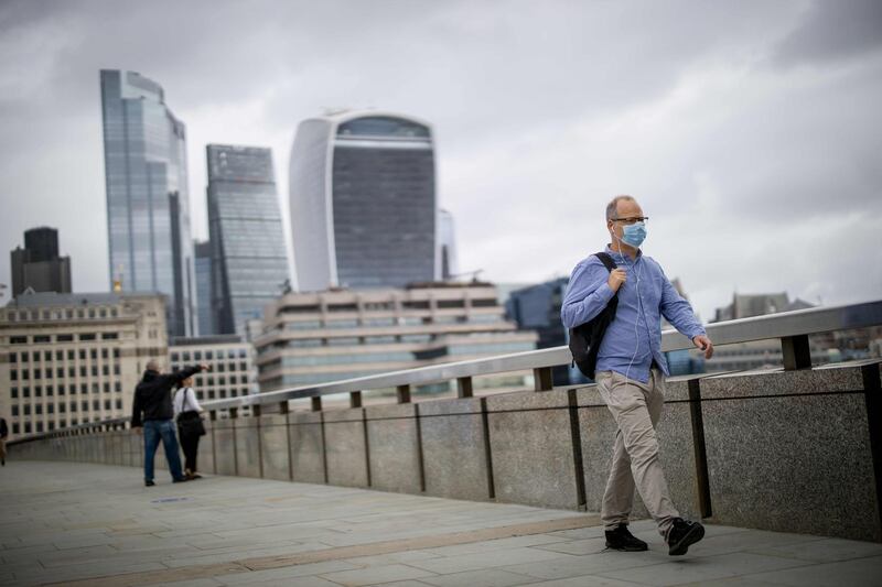 A man wearing a facemask as a precaution against the spread of the novel coronavirus walks across London Bridge with the offices of the City of London in Shard tower in the background on August 21, 2020. British government debt has exceeded £2.0 trillion for the first time following large state borrowing as the coronavirus pandemic pushed the UK economy deep into recession, official data showed on August 21. / AFP / Tolga Akmen

