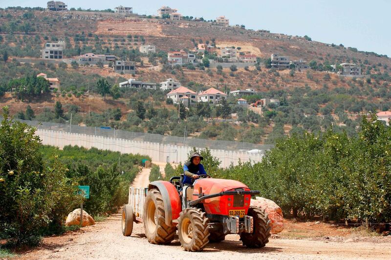 A farmer in the northern Israeli town of Metula drives his tractor in front of the concrete barrier along the border with Lebanon. AFP