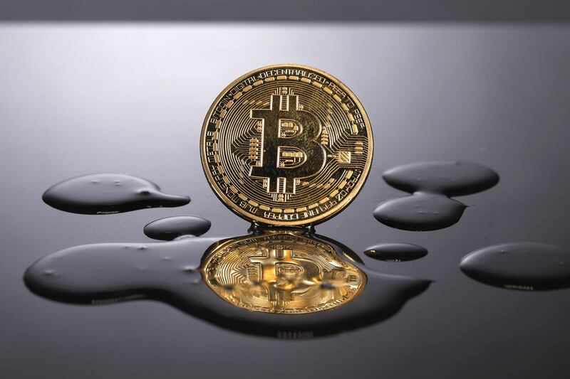 A coin representing Bitcoin cryptocurrency is reflected on a polished surface as it sits in a pool of translucent liquid in this arranged photograph in London, U.K., on Thursday, Feb. 8, 2018. Cryptocurrencies tracked by Coinmarketcap.com have lost more than $500 billion of market value since early January as governments clamped down, credit-card issuers halted purchases and investors grew increasingly concerned that last year’s meteoric rise in digital assets was unjustified. Photographer: Luke MacGregor/Bloomberg