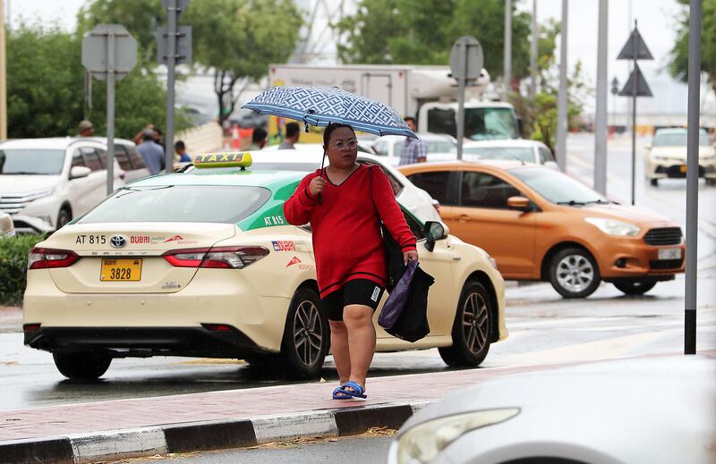 A person seeks shelter under an umbrella during the rain in Dubai. Pawan Singh / The National 