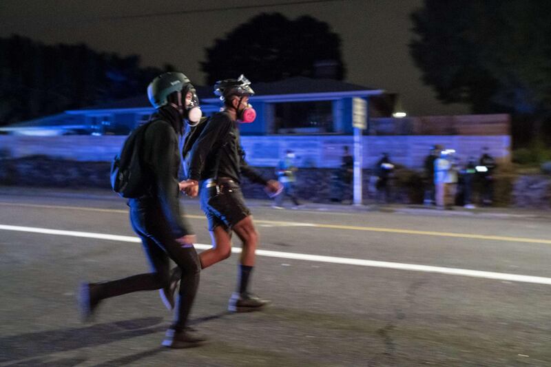 Two protesters run from police while holding hands during a march against police brutality and racial injustice in Portland, Oregon.  AFP