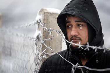 A migrant stands next to a fence during snowfall at the Lipa camp in Bosnia. AP