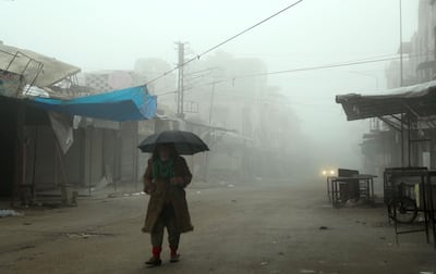 TOPSHOT - A man walks with an umbrella through a deserted foggy street in Maaret Al-Numan in the northwestern Idlib province on December 24, 2019, as government forces advance on the town. Syrian government forces on December 24 were less than four kilometres (two miles) from the strategic Maaret al-Numan, the head of the Britain-based monitor, Rami Abdel Rahman, told AFP. Fearing further advances, thousands of Maaret al-Numan's residents have fled.  / AFP / Omar HAJ KADOUR
