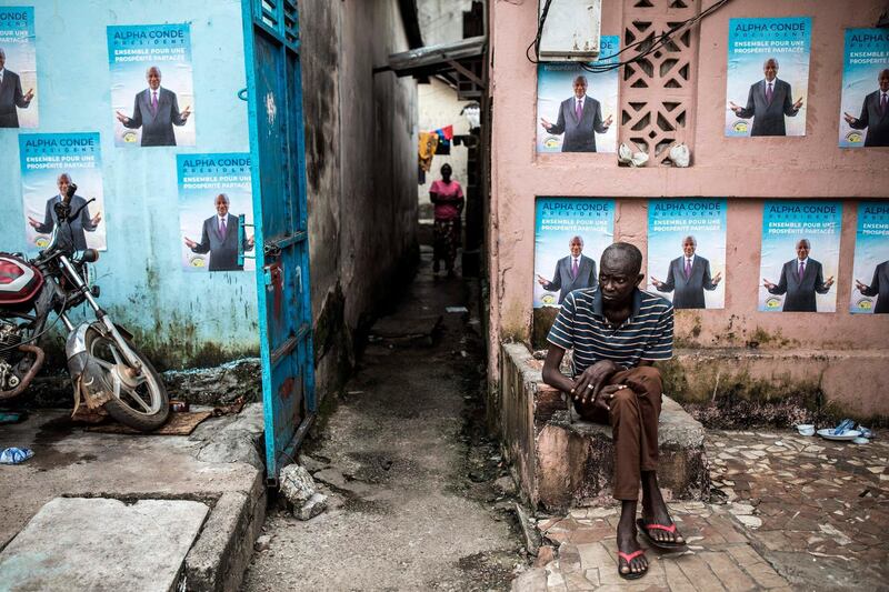 A man sits in front of campaign posters of President Alpha Conde in Conakry, Guinea. AFP