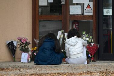TOPSHOT - Youngsters sit in front of flowers displayed at the entrance of a middle school in Conflans Saint-Honorine, 30kms northwest of Paris, on October 17, 2020, after a teacher was decapitated by an attacker who has been shot dead by policemen. The man suspected of beheading on October 16 ,2020 a French teacher who had shown his students cartoons of the prophet Mohammed was an 18-year-old born in Moscow and originating from Russia's southern region of Chechnya, a judicial source said on October 17. Five more people have been detained over the murder on October 16 ,2020 outside Paris, including the parents of a child at the school where the teacher was working, bringing to nine the total number currently under arrest, said the source, who asked not to be named. The attack happened at around 5 pm (1500 GMT) near a school in Conflans Saint-Honorine, a western suburb of the French capital. The man who was decapitated was a history teacher who had recently shown caricatures of the Prophet Mohammed in class. / AFP / Bertrand GUAY