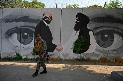 TOPSHOT - A security personnel walks past a wall mural with images of US Special Representative for Afghanistan Reconciliation Zalmay Khalilzad (L) and Taliban co-founder Mullah Abdul Ghani Baradar, in Kabul on July 31, 2020. Afghans offered prayers marking the Muslim festival of Eid al-Adha on July 31 as a three-day ceasefire between Taliban and government forces began, with many hoping the truce will lead to peace talks and the end of nearly two decades of conflict. / AFP / WAKIL KOHSAR
