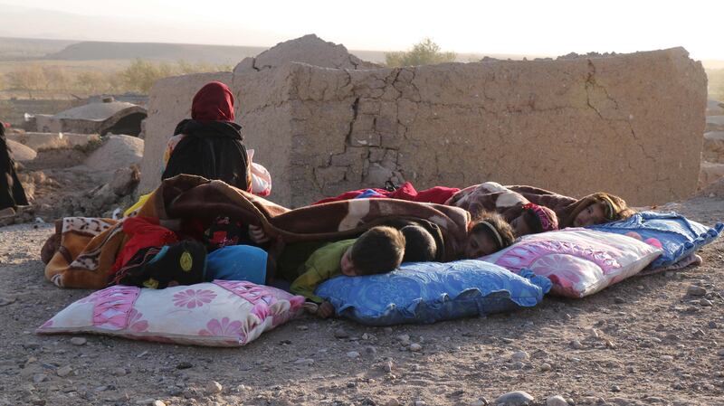 Afghan children rest under a blanket beside damaged houses after the earthquake. AFP