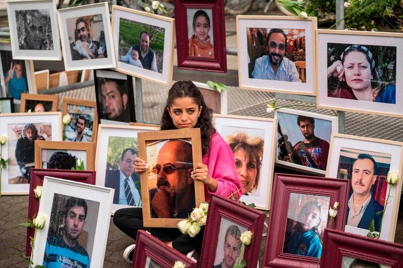 Syrian campaigner Wafa Mustafa sits between pictures of victims of the Syrian regime as she holds a picture of her father, during a protest outside the trial against two Syrian alleged former intelligence officers accused for crimes against humanity, in the first trial of its kind to emerge from the Syrian conflict, on June 4, 2020 in Koblenz, western Germany. Wafa was part of the resistance against the Syrian government and had to flee Syria once her dad was arrested. She came to Germany in 2016. / AFP / Thomas Lohnes
