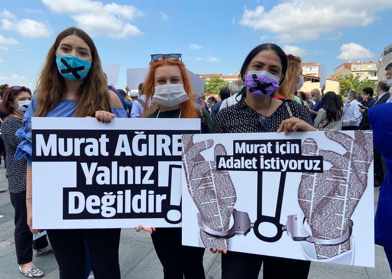 People hold placards that read " Murat Agirel is not alone " and " we want justice for Murat " outside the courthouse, in Istanbul, Wednesday, June 24, 2020. Seven journalists went on trial on Wednesday, accused of revealing state secrets for their reports on the funeral an intelligence officer who was killed in Libya. (AP Photo/Mehmet Guzel)