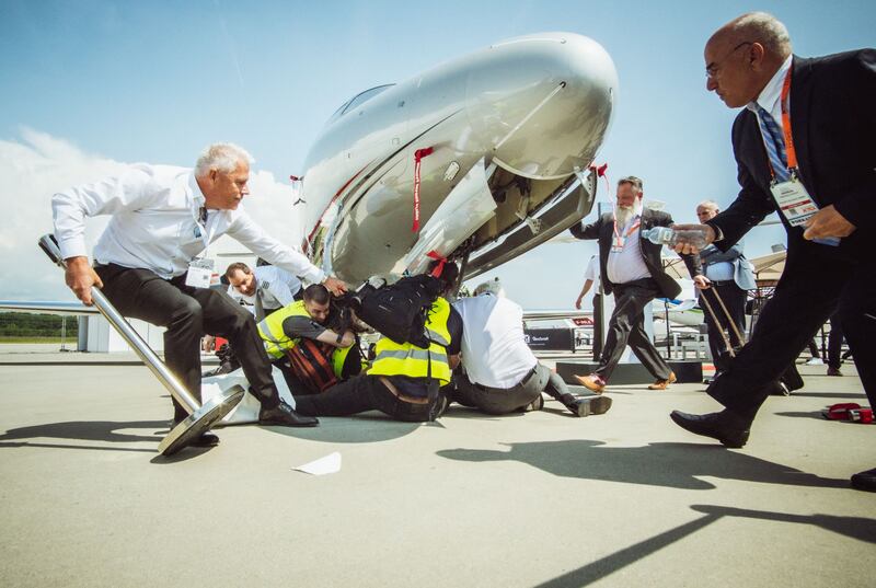 This handout picture taken and released on May 23, 2023 by Greenpeace shows unidentified people rushing to climate activists beneath a business jet during a protest at European business aviation show EBACE (European Business Aviation Convention & Exhibition) at Geneva Airport on May 23, 2023.  Protesters on the tarmac at Geneva airport briefly disrupted air traffic before operations were gradually resumed, the airport said, as dozens of climate activists blocked a nearby business jet convention.  (Photo by Thomas Wolf  /  GREENPEACE  /  AFP)  /  RESTRICTED TO EDITORIAL USE - MANDATORY CREDIT "AFP PHOTO  /  GREENPEACE  /  THOMAS WOLF" -  TO ILLUSTRATE THE EVENT AS SPECIFIED IN THE CAPTION - NO MARKETING NO ADVERTISING CAMPAIGNS - DISTRIBUTED AS A SERVICE TO CLIENTS - NO ARCHIVE