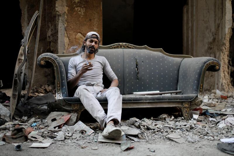 Refugee Abu Nimr, 36, smokes a cigarette as he sits on a sofa along a damaged street in Yarmouk, a Palestinian camp in Damascus, Syria. REUTERS