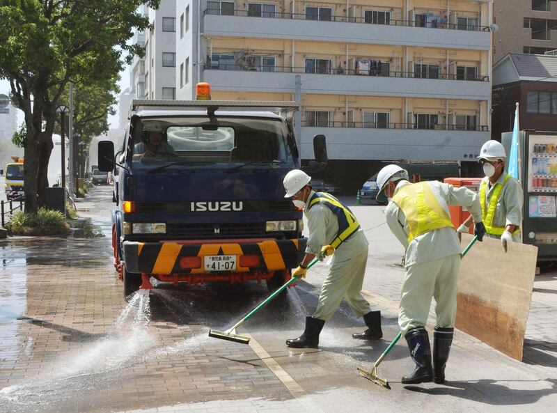 City officials wearing masks clean the pavement covered by ash Monday morning, Aug. 19, 2013 after the Sakurajima volcano erupted Sunday afternoon in Kagoshima, on the southern Japanese main island of Kyushu. People in the city wore masks and raincoats and used umbrellas to shield themselves from the ash after the eruption. (AP Photo/Kyodo News) JAPAN OUT, MANDATORY CREDIT *** Local Caption ***  Japan Volcano.JPEG-04c39.jpg