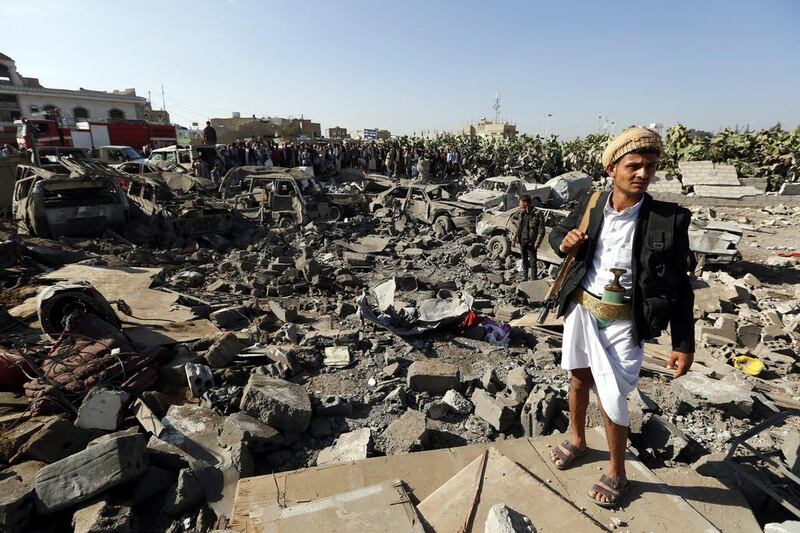 An armed member of the Houthis keeps watch as people gather beside vehicles which were destroyed by a Saudi air strike, in Sanaa, Yemen on March 26, 2015. Yahya Arhab/EPA