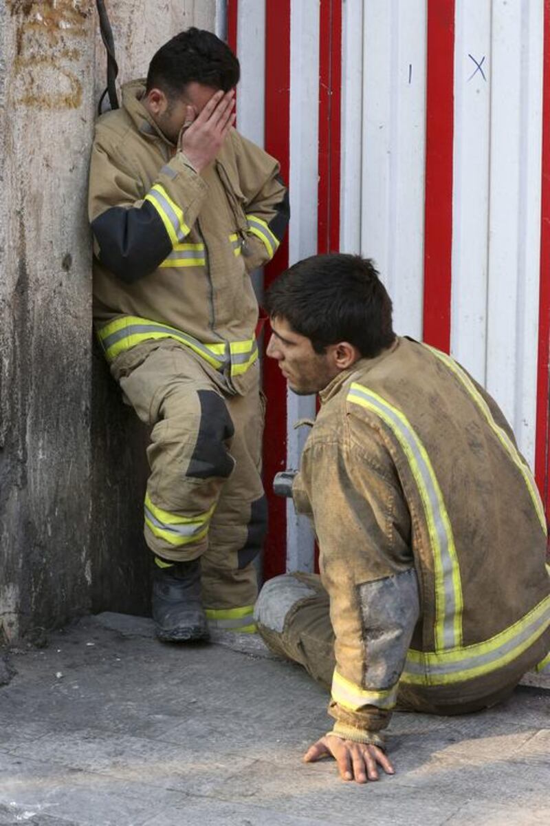 A firefighter sits next to his colleague on January 19, 2017, outside the historic Plasco building in Tehran, Iran. The iconic structure was destroyed by a fire on Thursday. Dozens of firefighters were killed when the building collapsed. Vahid Salemi / Associated Press