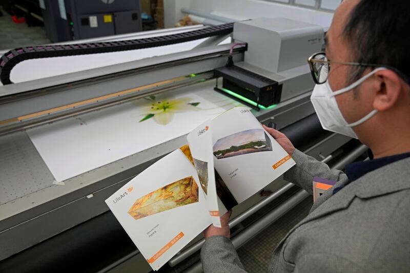 Mr Tong looks at a catalogue showing more than 40 different choices of coffin designs as a machine prints the lily design.