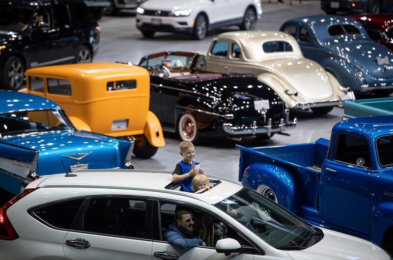Children stand through a sunroof while attending a drive-though classic and custom car show on the arena floor at Pacific Coliseum, in Vancouver, British Columbia. The Canadian Press via AP