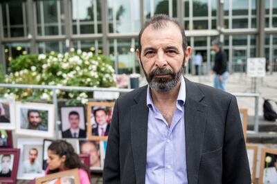 Syrian human rights lawyer Anwar al-Bunni, speaks to the media in front of pictures of victims of the Syrian regime, during a protest outside the trial against two Syrian alleged former intelligence officers accused for crimes against humanity, in the first trial of its kind to emerge from the Syrian conflict, on June 4, 2020 in Koblenz, western Germany. (Photo by Thomas Lohnes / AFP)