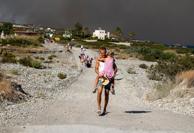 A man carries a child as they leave an area where a forest fire burns. AP 