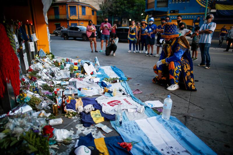 A fan mourns in front of flowers and posters left in tribute to Maradona at the entrance of the Boca Juniors stadium. AP