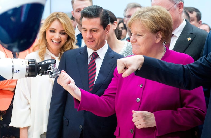 German chancellor Angela Merkel fist bumps a robot Mexican president Enrique Pena Nieto and his wife Angelica Rivera look on at the Hanover Fair in Hanover. Hauke-Christian Dittrich / dpa / AFP Photo