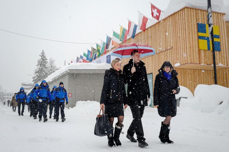 People walk through the resort town of Davos as snow falls ahead of the World Economic Forum (WEF) 2018 annual meeting, on January 22, 2018 in Davos, eastern Switzerland. / AFP PHOTO / Fabrice COFFRINI