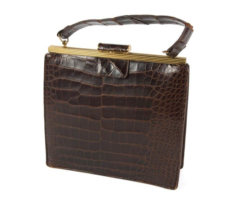 A chocolate brown 1950s alligator handbag features gold metal hardware and burgundy leather interior with purpose-built pockets to accommodate matching accessories. Courtesy Julien's Auctions