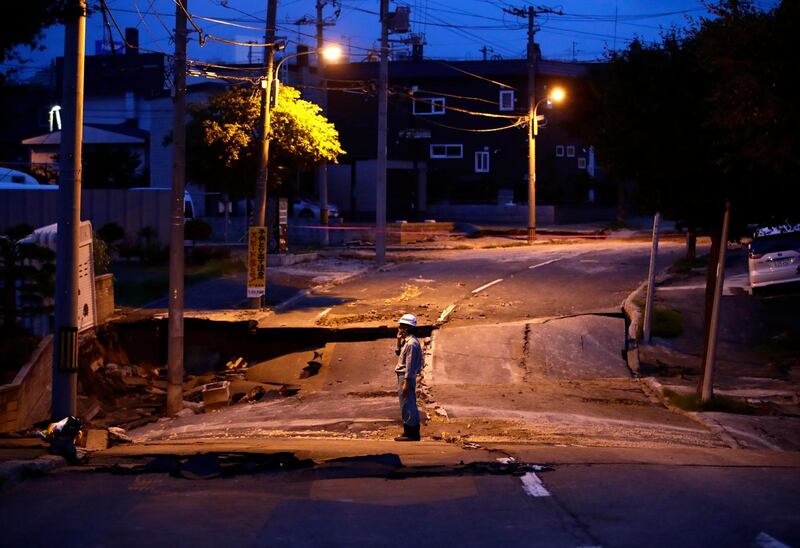 A security guard stands on the earthquake-damaged street in Kiyota, on outskirts of Sapporo city, Hokkaido, northern Japan. AP