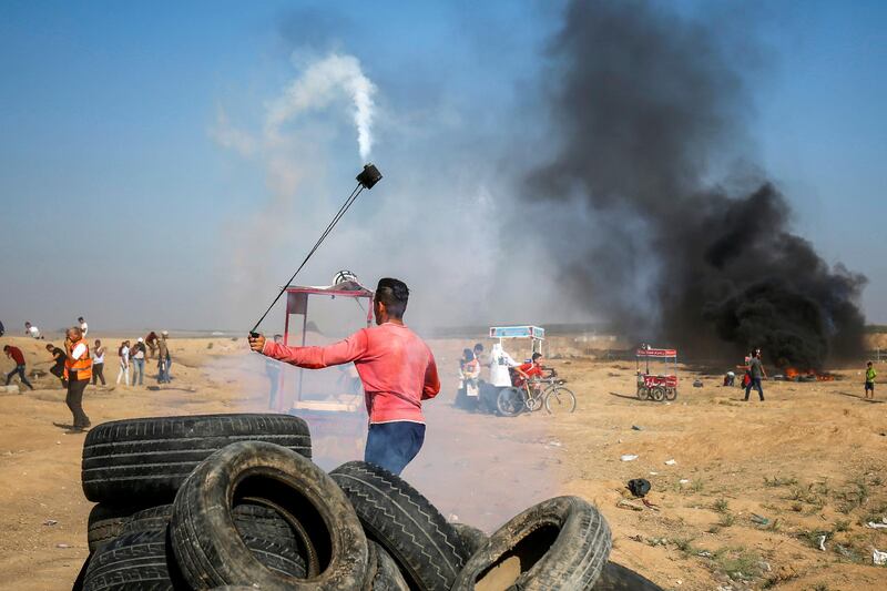A Palestinian protester uses a slingshot to throw back a tear gas canister towards Israeli forces during clashes following a demonstration along the border east of Gaza City on July 6, 2018.  / AFP / SAID KHATIB
