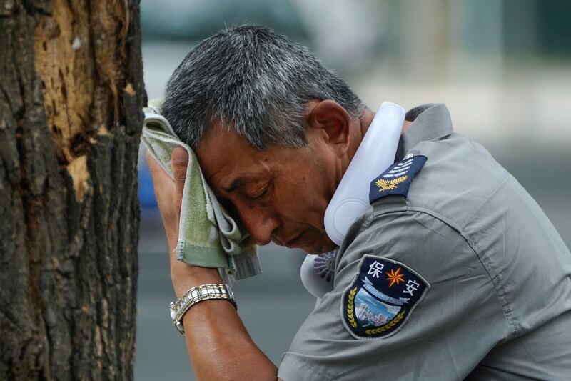 A security guard wearing an electric fan on his neck wipes his brow in Beijing on Monday. AP