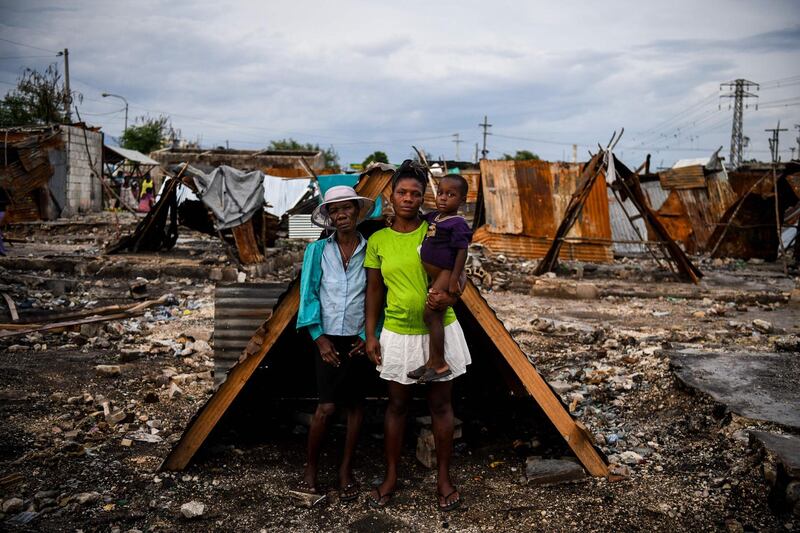 Three friends pose outside a makeshift shelter on the site of their home which was burned during a gang war in Port-au-Prince, Haiti. AFP