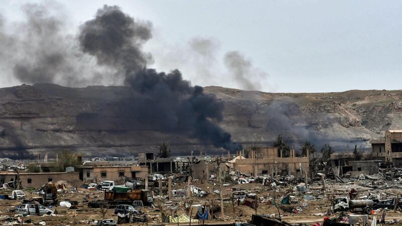 This picture taken on March 24, 2019 shows smoke rising behind destroyed vehicles and damaged buildings in the village of Baghouz in Syria's eastern Deir Ezzor province near the Iraqi border, a day after the Islamic State (IS) group's "caliphate" was declared defeated by the US-backed Kurdish-led Syrian Democratic Forces (SDF). (Photo by GIUSEPPE CACACE / AFP)