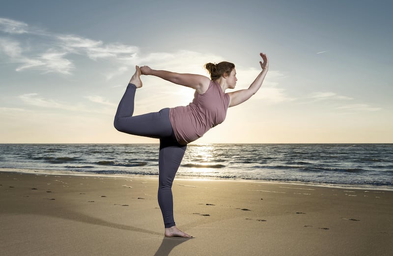 Mature woman practising yoga on a beach at sunset, tree pose