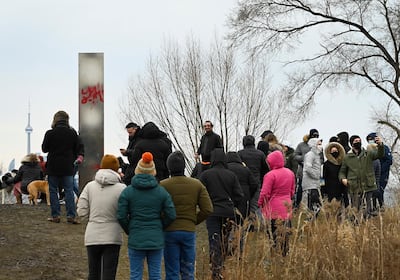 People look at a metallic monolith that appeared on the shorelines of Humber Bay Park during the COVID-19 pandemic in Toronto on Friday, Jan. 1, 2021. (Nathan Denette/The Canadian Press via AP)