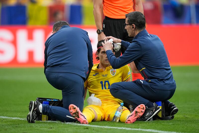 Romania's Ianis Hagi receives attention from the medical staff after taking a knock to the head. AP