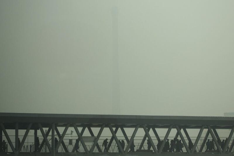 A chimney of a heating plant is obscured by heavy haze as commuters walk through a bridge linking a subway station and a bus station on a severely polluted day in Beijing on February 25. Beijing remained cloaked in hazardous white pollution hiding much of its skyline on Tuesday. Alexander F. Yuan/AP 