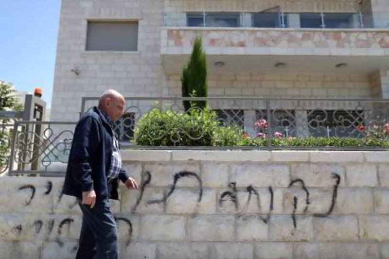 A Palestinian man walks past graffiti painted on a wall outside a house in Hebrew reading "price tag" near where two vehicles were torched in the east Jerusalem neighborhood of Sheikh Jarrah.