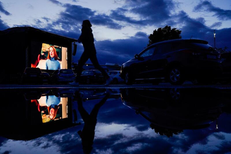 A visitor walks on a parking lot in front of a screen in the drive-in cinema of the Technik Museum in Speyer, Germany. dpa via AP