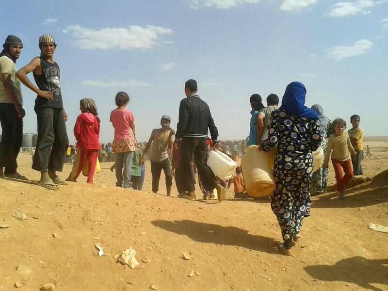 FILE - In this June 23, 2016 file photo, Syrian refugees gather for water at the informal Rukban camp for displaced Syrians, between the Jordan and Syria borders. Desperate to help Syrians stuck on Jordan's sealed border, U.N. agencies reluctantly agreed late last year to hand much of the control over aid distribution to Jordan's military, a Jordanian contractor and a Syrian militia. Since then, the system has broken down repeatedly and only sporadic aid shipments have reached the two remote desert camps on the border. (AP Photo, File)