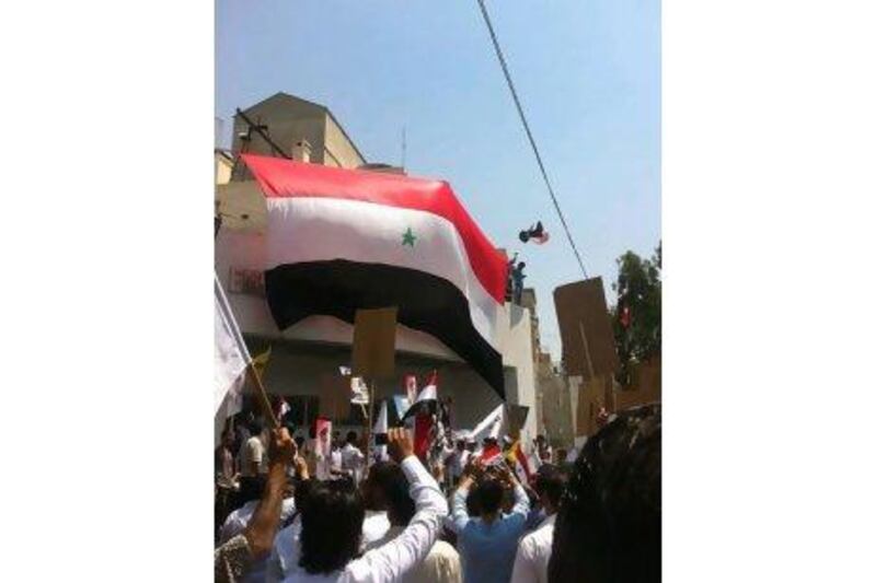 Pro-Assad demonstrators hang a huge Syrian flag at the entrance of the US embassy compound in Damascus as they protest against the US ambassador, Robert Ford, after his visit to the Syrian city of Hama.