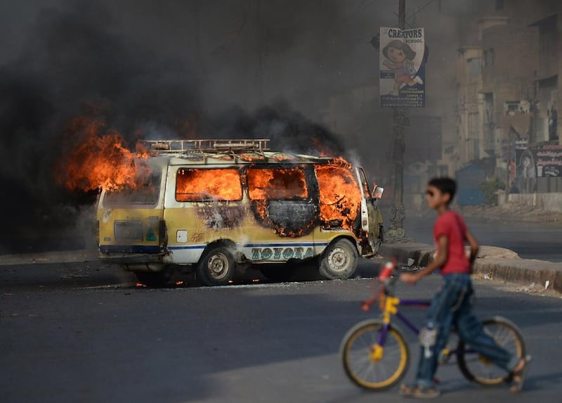 A Pakistani youth wheels his bicycle past a burning vehicle on a street in Karachi on Tuesday following the arrest of Altaf Hussain, head of Pakistan's Muttahida Qaumi Movement party, in London. Asif Hassan / AFP

