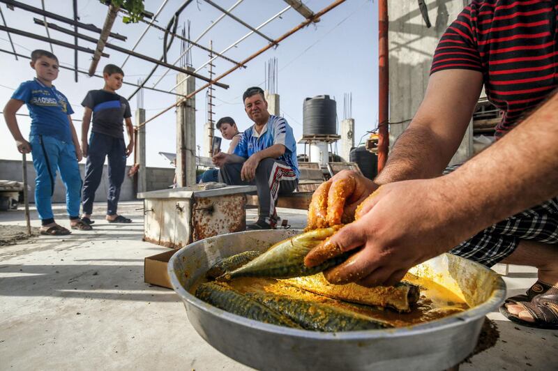 Palestinian family members prepare to smoke mackerel on the roof of their house in preparation for the upcoming Eid al-Fitr holiday which marks the end of the Islamic holy month of Ramadan, in the southern Gaza Strip city of Rafah on May 19, 2020. (Photo by SAID KHATIB / AFP)